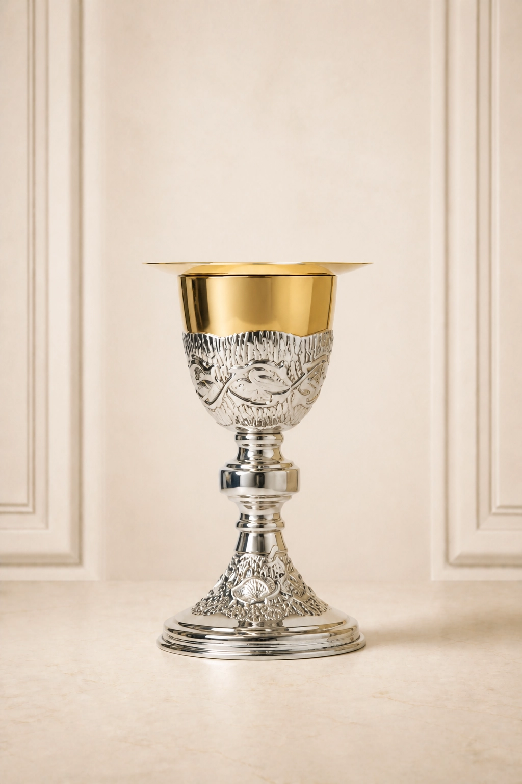 Cáliz litúrgico bicolor con patena superior, borde dorado, relieves figurativos en la copa y base acampanada ornamentada