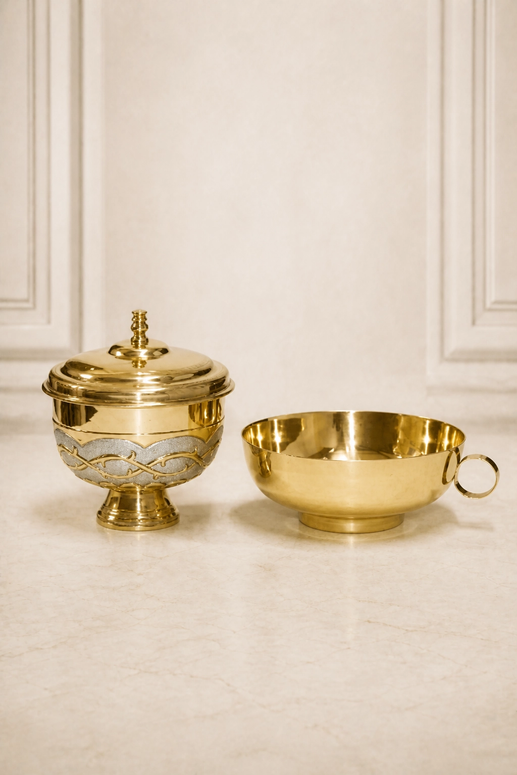 Conjunto litúrgico dorado con copón de franja plateada y relieve de corona de espinas junto a un cuenco con asa lateral